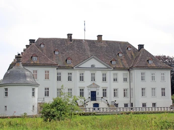 Wasserschloss Vinsebeck mit symmetrischer Fassade und Erkerturm, umgeben von grüner Landschaft.