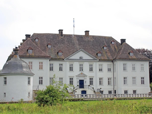 Wasserschloss Vinsebeck mit symmetrischer Fassade und Erkerturm, umgeben von grüner Landschaft.