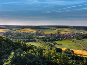 Blick auf Höhendörfer Panoramablick über sanfte Hügel und Felder, gesäumt von dichten Wäldern unter blauem Himmel.