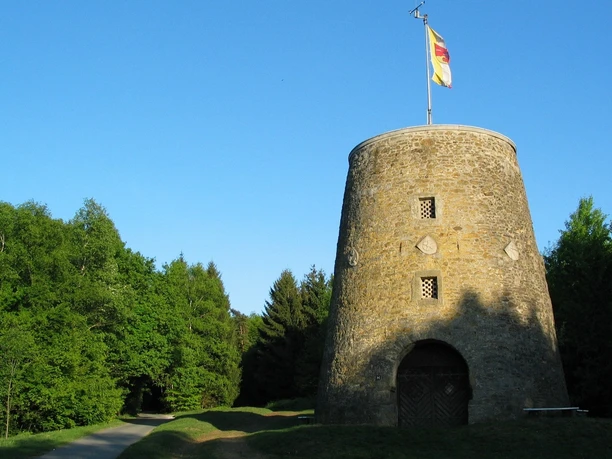 Kumsttonne Oerlinghausen Alte Mühle in Oerlinghausen, ohne Flügel, im Grünen, mit Deutschlandfahne an klarblauem Himmel.