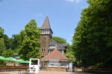 Wittekindsburg Historisches Fachwerkgebäude mit spitzem Turm, umgeben von grünen Bäumen und einem Biergarten.