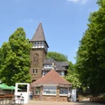 Wittekindsburg Historisches Fachwerkgebäude mit spitzem Turm, umgeben von grünen Bäumen und einem Biergarten.