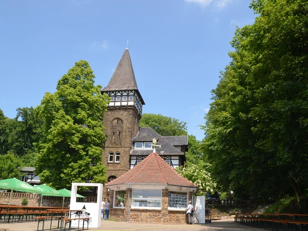 Wittekindsburg Historisches Fachwerkgebäude mit spitzem Turm, umgeben von grünen Bäumen und einem Biergarten.