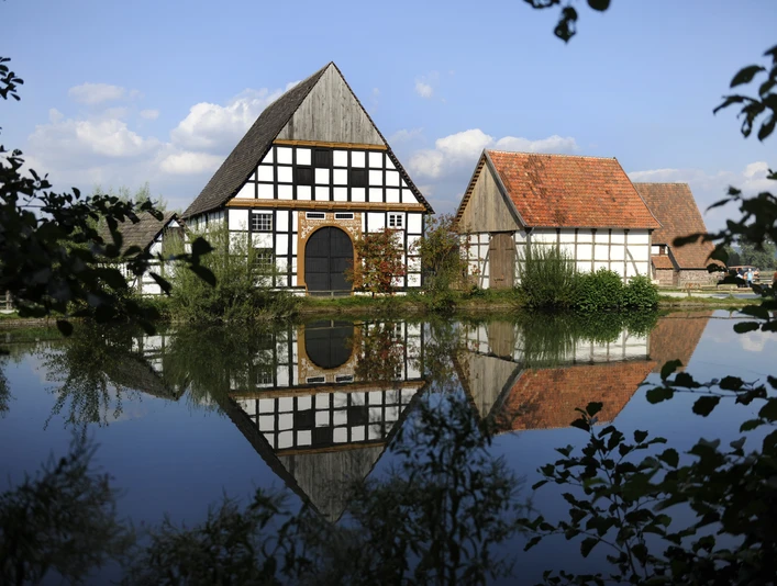 Der Dorfteich des LWL-Freilichtmuseums Detmold. Der Dorfteich im LWL-Freilichtmuseum Detmold spiegelt Fachwerkhäuser und bewölkten Himmel wider.