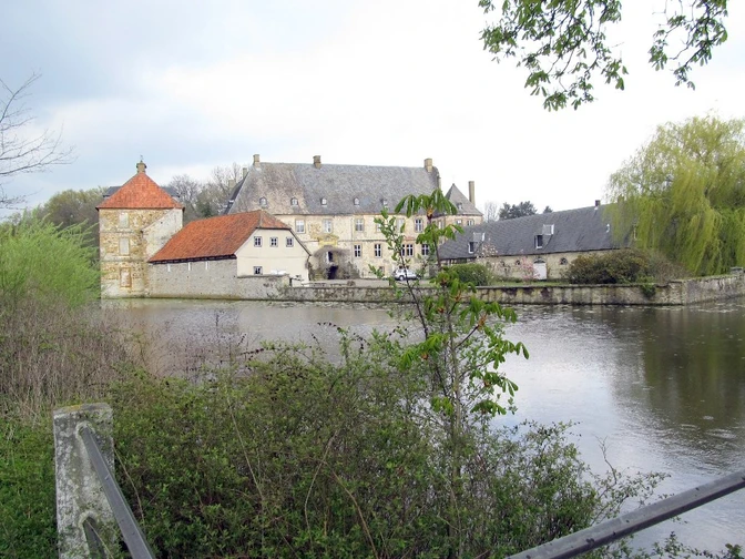 Wasserschloss Tatenhausen Historisches Wasserschloss reflektiert im ruhigen Weiher, umrahmt von grüner Vegetation und Bäumen.