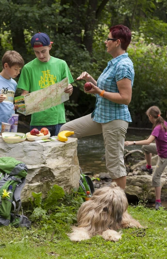 Eine Familie mit Rucksäcken pausiert in der Natur, studiert eine Karte, während Hunde entspannen.