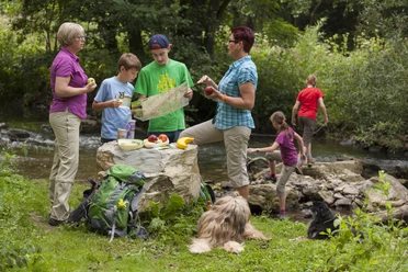 Eine Familie mit Rucksäcken pausiert in der Natur, studiert eine Karte, während Hunde entspannen.