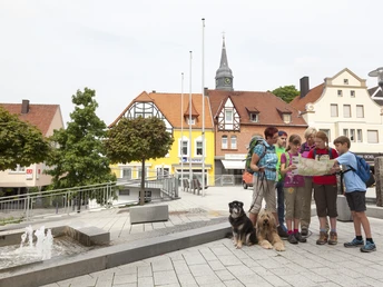 Eine wandernde Familie mit Landkarte auf dem Bürener Marktplatz, umgeben von historischen Gebäuden.