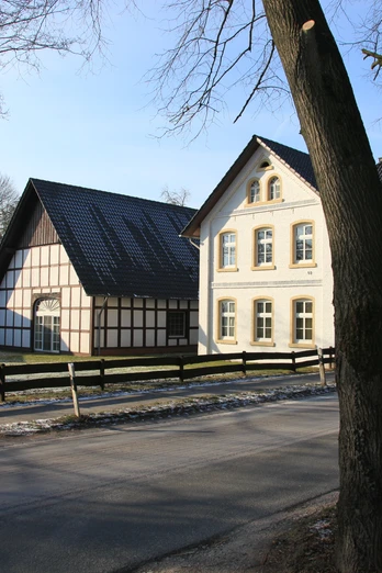 image Historisches Fachwerkgebäude mit großen Fenstern und schwarzem Dach, umgeben von Bäumen.