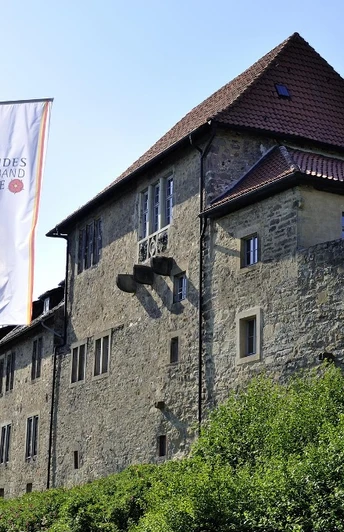 Historische Burg Sternberg mit markanten Steinfassaden und drei großen weißen Fahnen im Vordergrund.