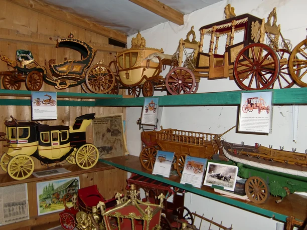 Mühlenmuseum In einem Museum sind auf Holzregalen Modelle historischer Kutschen und Wägen ausgestellt.