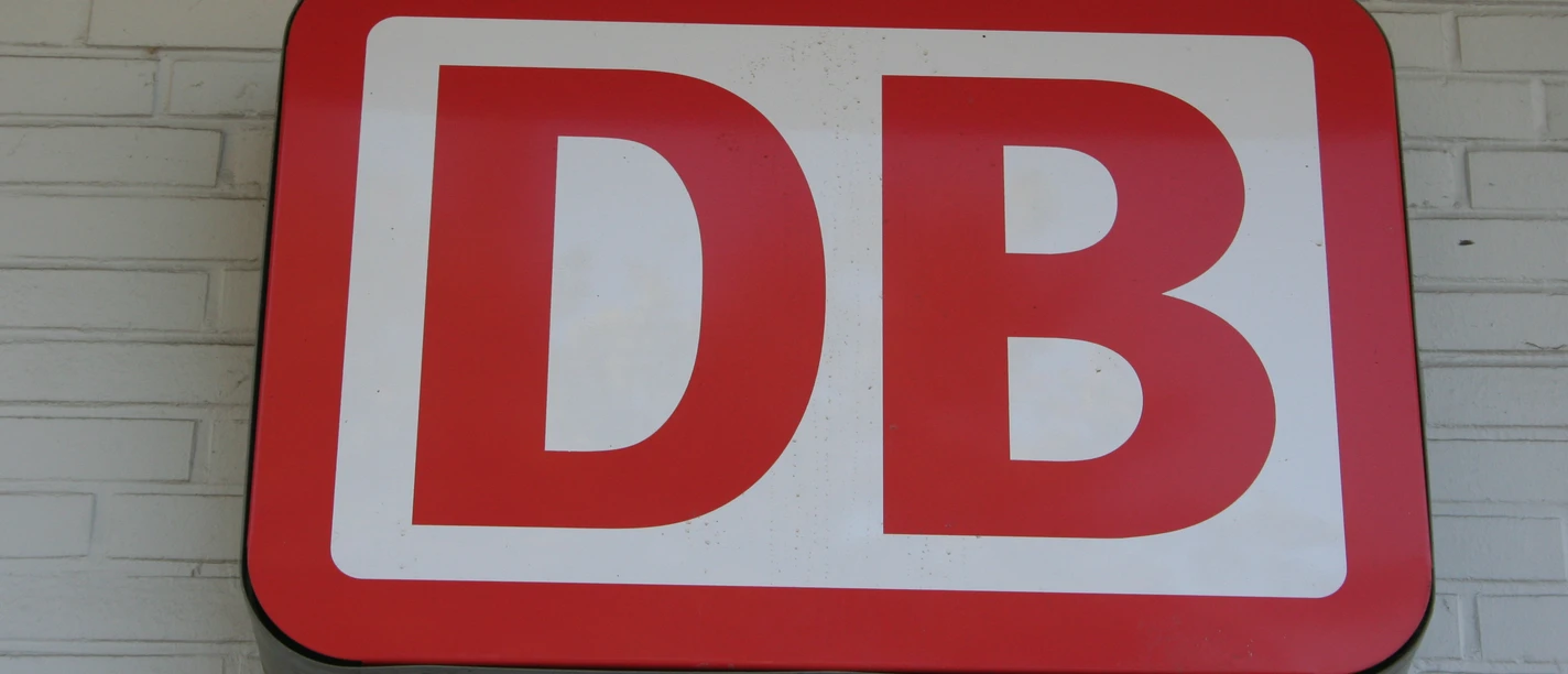 Rotes DB-Logo der Deutschen Bahn auf heller Ziegelwand montiert. Symbol für den Schienenverkehr.