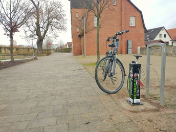 Fahrrad steht an einer Reparaturstation im Emmerauenpark Lügde, neben einer gepflasterten Allee.