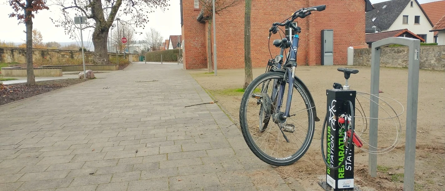 Die Fahrradreparaturstaion im Lügder Emmerauenpark Fahrrad steht an einer Reparaturstation im Emmerauenpark Lügde, neben einer gepflasterten Allee.