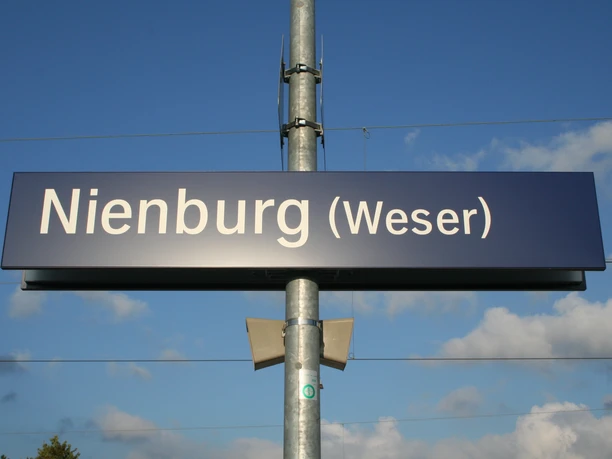 Bahnhof Nienburg Bahnhofsschild von Nienburg (Weser) an einem sonnigen Tag mit blauen Himmel und vereinzelten Wolken.