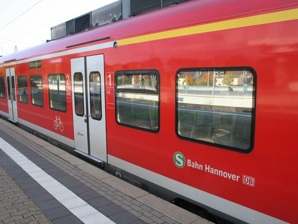 Eine rote S-Bahn der Deutschen Bahn steht am sonnigen Gleis, Türen geschlossen, Fahrradabteil markiert.