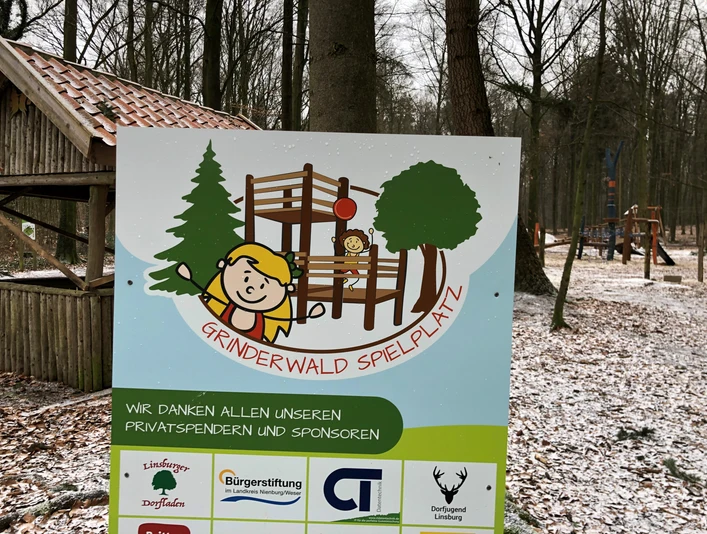 Ein verschneiter Spielplatz im Grinderwald, umgeben von Bäumen, mit Holzklettergerüst und Schaukeln.