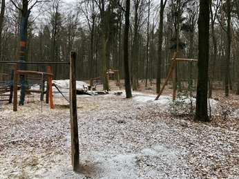 Grinderwald Spielplatz Verschneiter Waldspielplatz mit Klettergerüst, gesäumt von hohen Bäumen und natürlicher Umgebung.