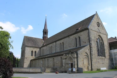 Kloster Loccum Mittelalterliche Klosterkirche aus Stein mit rotem Turm vor blauem Himmel, umgeben von Gärten.
