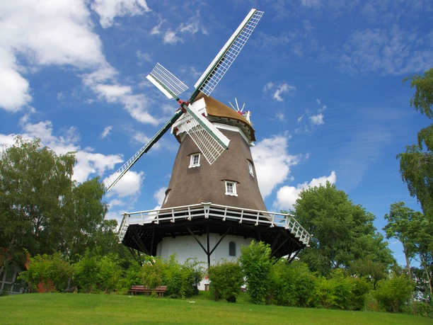 Historische windmolen in Achim met wit hekwerk en roodgekleurd dak, omringd door bomen.