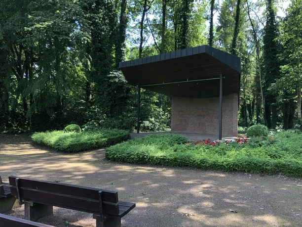 Een overdekt podium in het kuurpark Bruchhausen-Vilsen, omgeven door groene vegetatie en parkbankjes.
