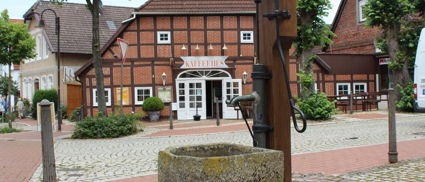 Ortsmitte Bruchhausen-Vilsen Historic half-timbered house with "KAFFEEHAUS" lettering, surrounded by cobblestones and trees.