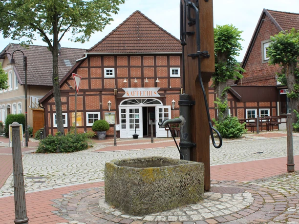 Ortsmitte Bruchhausen-Vilsen Historisches Fachwerkhaus mit Schriftzug "KAFFEEHAUS", umgeben von Pflastersteinen und Bäumen.