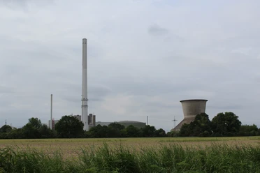 Landesbergen Kraftwerk Kraftwerk mit hohem Schornstein und Kühlturm umgeben von grünen Feldern und Bäumen an bewölktem Himmel.
