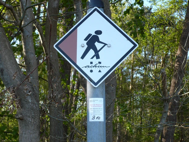 Wandelwegwijzer in het heidegebied met pictogram van een wandelaar en het opschrift "Achim".