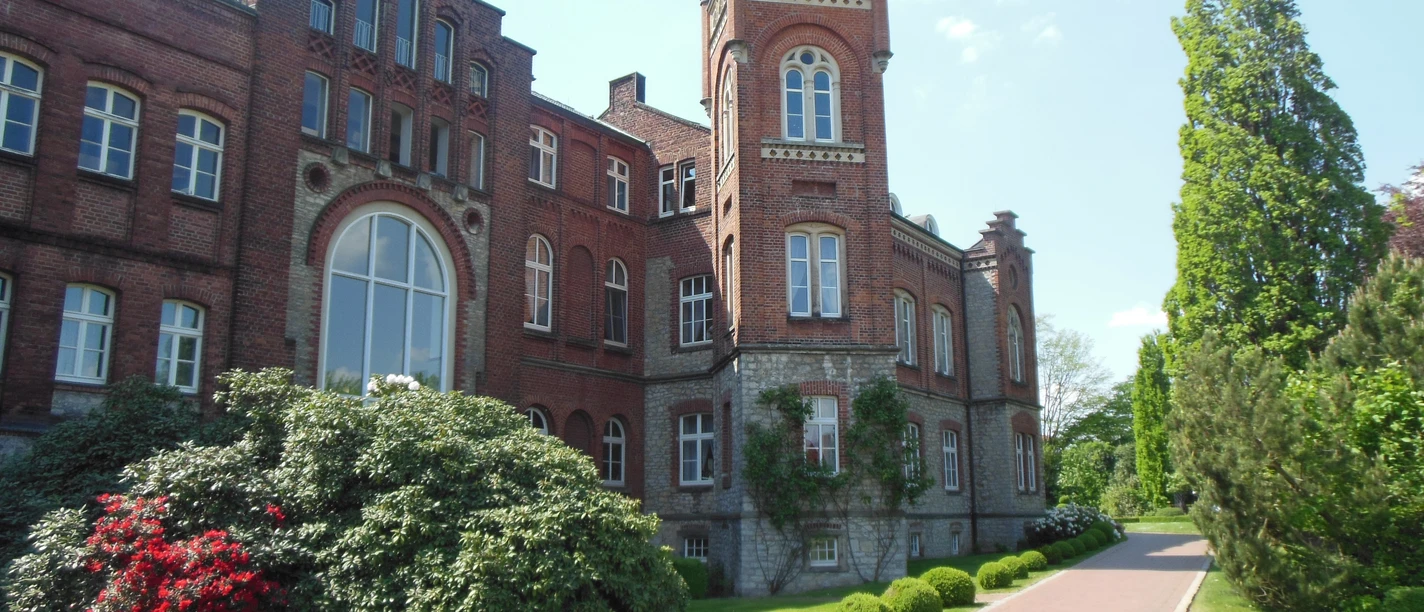 Historische Backstein-Brauerei mit Türmchen, großen Fenstern, umgeben von gepflegtem Grün und Rosen.