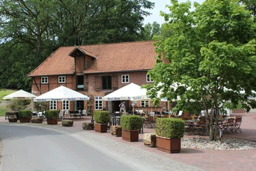 Historische Backsteinmühle mit Biergarten, Holztischen und weißen Sonnenschirmen unter blühendem Baum.