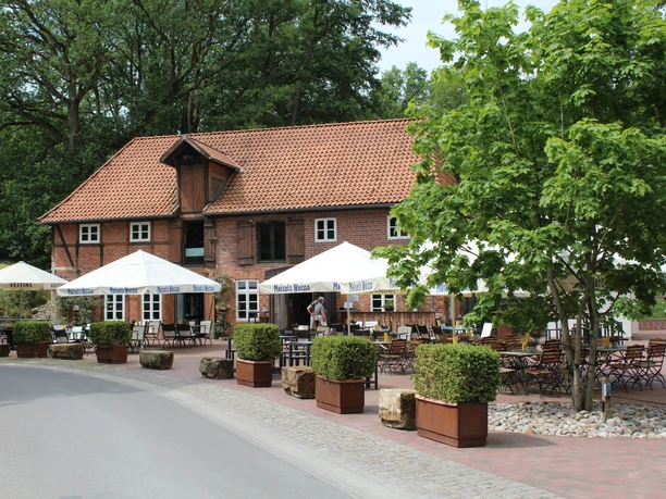 Klostermühle Heiligenberg Historische Backsteinmühle mit Biergarten, Holztischen und weißen Sonnenschirmen unter blühendem Baum.