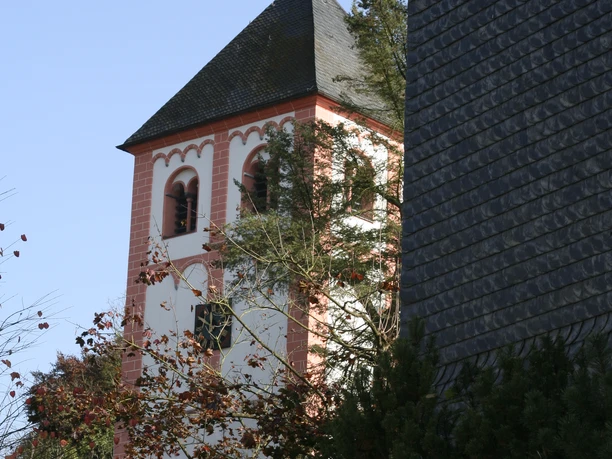 Kirchturm St. Pankratius Odenthal Der gotische Kirchturm mit rot-weißen Details ragt zwischen Bäumen auf, bei klarem Himmel.