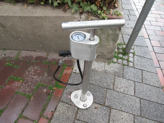 Lufttankstelle Lufttankstelle aus Metall mit Manometer und Schlauch auf gepflastertem Gehweg neben einem Betonrand.