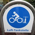 Ein Schild mit blauem Kreis und Piktogramm einer Person auf einem Fahrrad. Schrift: Luft-Tankstelle.