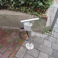 Luftstation mit Handpumpe für Fahrräder auf einem gepflasterten Bürgersteig, von Pflanzen umgeben.