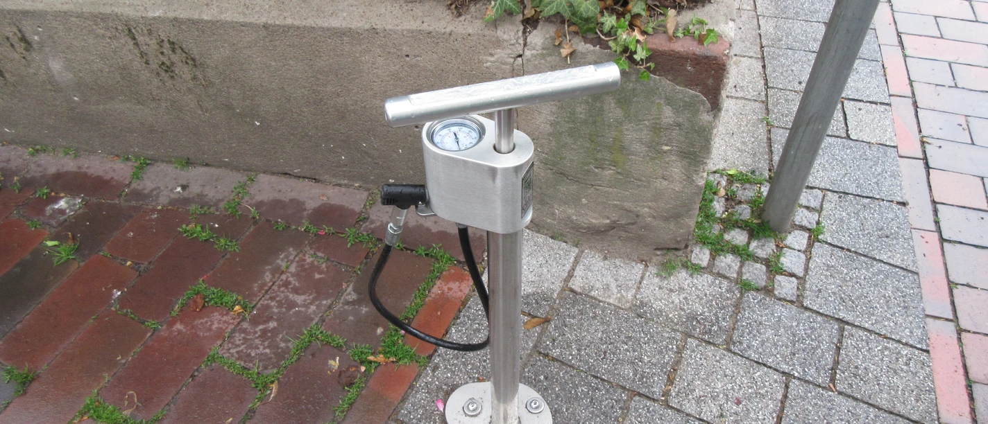Lufttankstelle Luftstation mit Handpumpe für Fahrräder auf einem gepflasterten Bürgersteig, von Pflanzen umgeben.