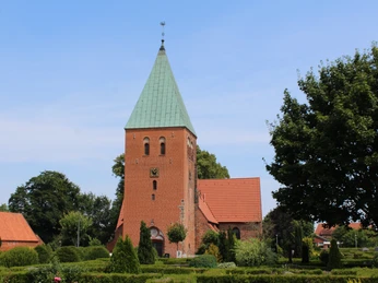 Kirche Riede Kirche Riede mit rotem Backsteinturm, grünem Spitzdach, umgeben von Bäumen und gepflegtem Garten.Riede church with red brick tower, green pointed roof, surrounded by trees and well-tended garden.Riede kirke med tårn af røde mursten, grønt spidst tag, omgivet af træer og en velplejet have.Riede kerk met rode bakstenen toren, groen puntdak, omgeven door bomen en een goed onderhouden tuin.