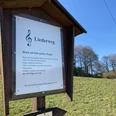 Liedertafel "Hoch auf dem Gelben Wagen" <p>Eine Tafel am Liederweg mit Notenschlüssel und Text im sonnigen Landschaftspanorama.</p>
