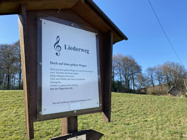 Liedertafel "Hoch auf dem Gelben Wagen" <p>Eine Tafel am Liederweg mit Notenschlüssel und Text im sonnigen Landschaftspanorama.</p>