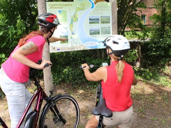 Weseraue Zwei Radfahrerinnen mit Schutzhelmen betrachten eine Karte im Vogel-schutzgebiet Weseraue.