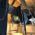 Antiker Reitsattel hängt in einem rustikalen Holzstall mit Strohballen und alten Holzbalken.