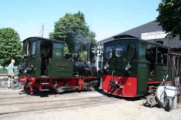 Museums-Eisenbahn Bruchhausen-Vilsen Zwei historische Dampflokomotiven stehen auf parallelen Gleisen vor einem Eisenbahnmuseum.