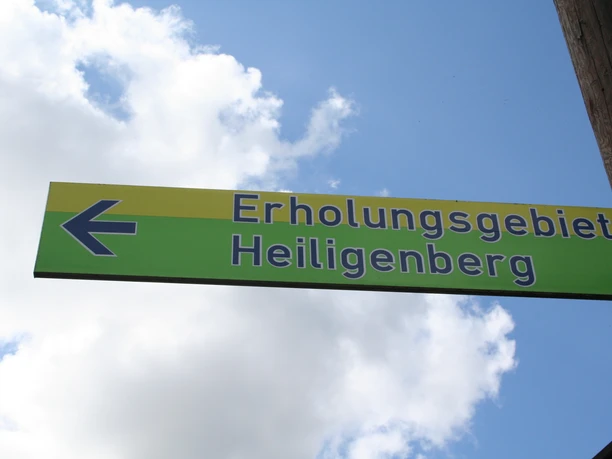 Een groen bord met een geel vlak en blauwe letters geeft het recreatiegebied Heiligenberg aan.