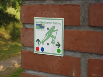 Nordic Walking Thedinghausen Wegweiser für Nordic Walking, befestigt auf einer Backsteinmauer, umgeben von grünem Laub.Signpost for Nordic walking, mounted on a brick wall, surrounded by green foliage.Skilt til stavgang, monteret på en murstensvæg, omgivet af grønne blade.Wegwijzer voor Nordic Walking, gemonteerd op een bakstenen muur, omgeven door groen gebladerte.