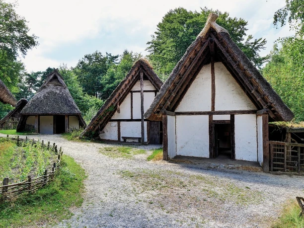 Historische Nachbildung: Traditionelle germanische Langhäuser mit Strohdächern in bewaldeter Freilichtanlage.