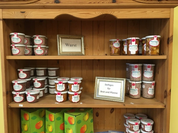 Produktauswahl Regal mit Gläsern voller Wurstspezialitäten und Apfelkartons im Hofladen Koch.