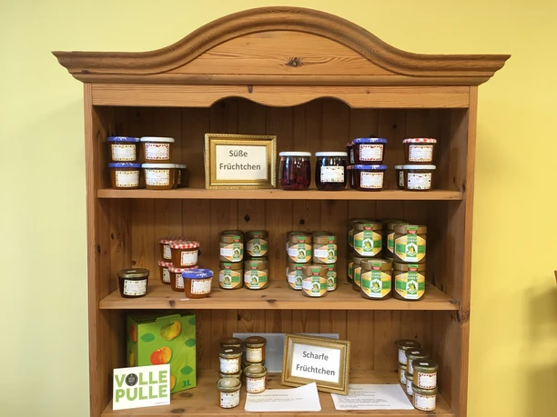 Holzregal mit Gläsern voller Marmelade, Honig und Chutneys sowie Apfelsaft.