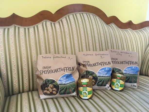 Drei Papiertüten mit Kartoffeln und zwei Gläser Honig stehen auf einem gestreiften Sofa.