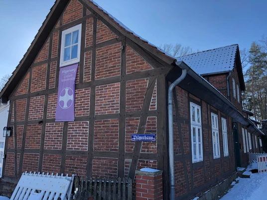 Rotes Backsteinhaus im Fachwerkstil, zweistöckig, im Winter; Banner "Pilgerweg Loccum Volkenroda".